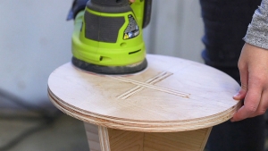 Man sanding round wood table with orbital sander