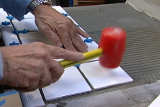 Tapping tiles into place with a plastic mallet
