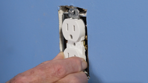 Man holding loose electrical outlet in electrical box