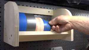 man pulling tape from wooden rack attached to pegboard
