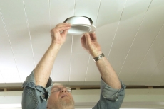 Man replaces light fixture on plank ceiling 