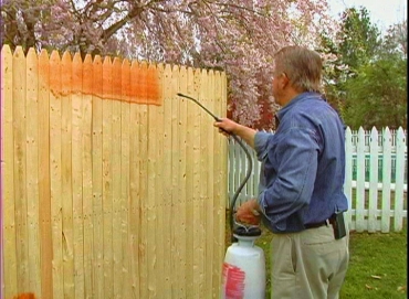 Man spraying exterior stain on wooden fence