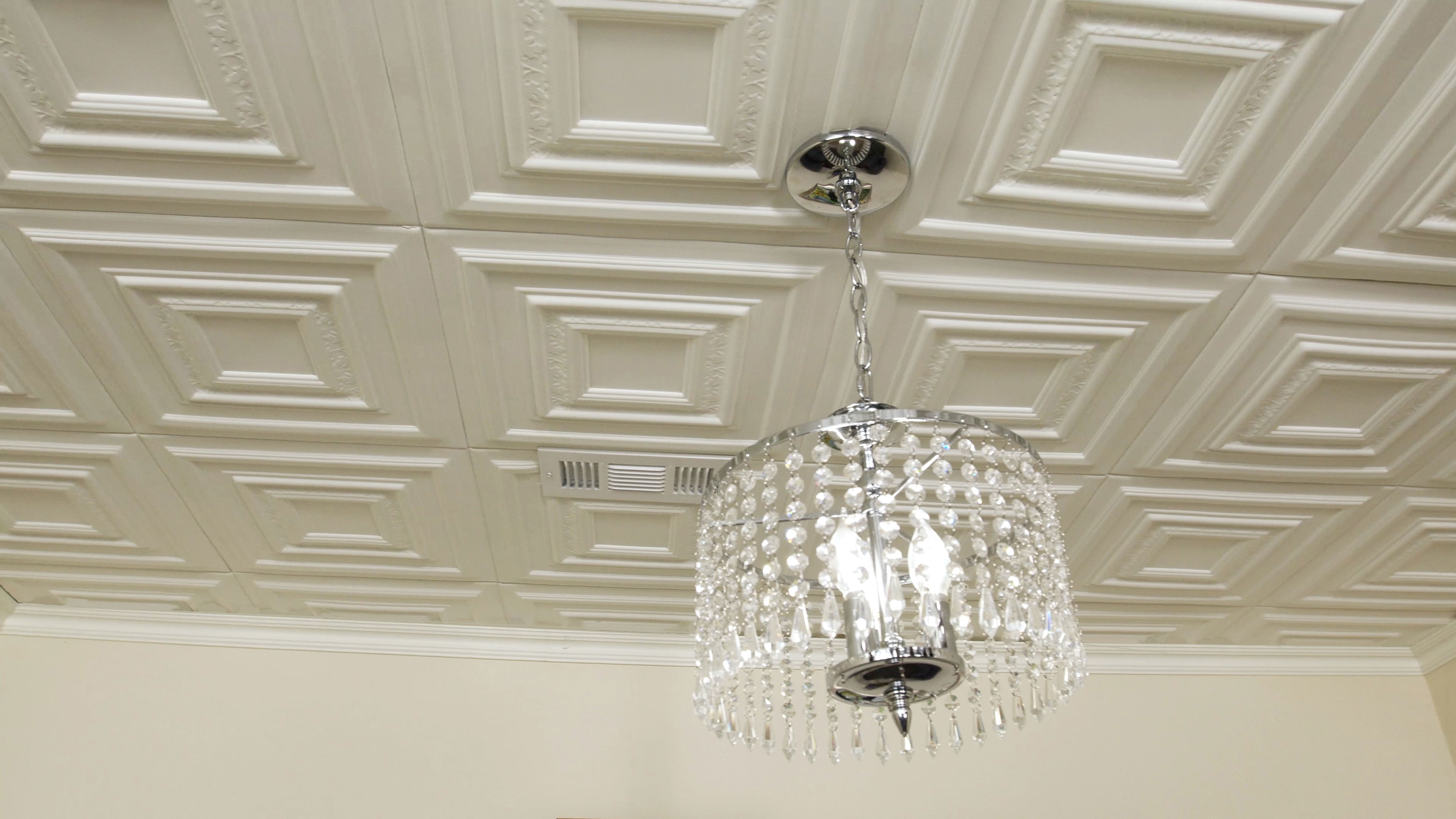 Silver and crystal chandelier hanging from foam tile ceiling