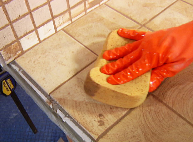 Gloved hand holding a sponge over grouted tile 