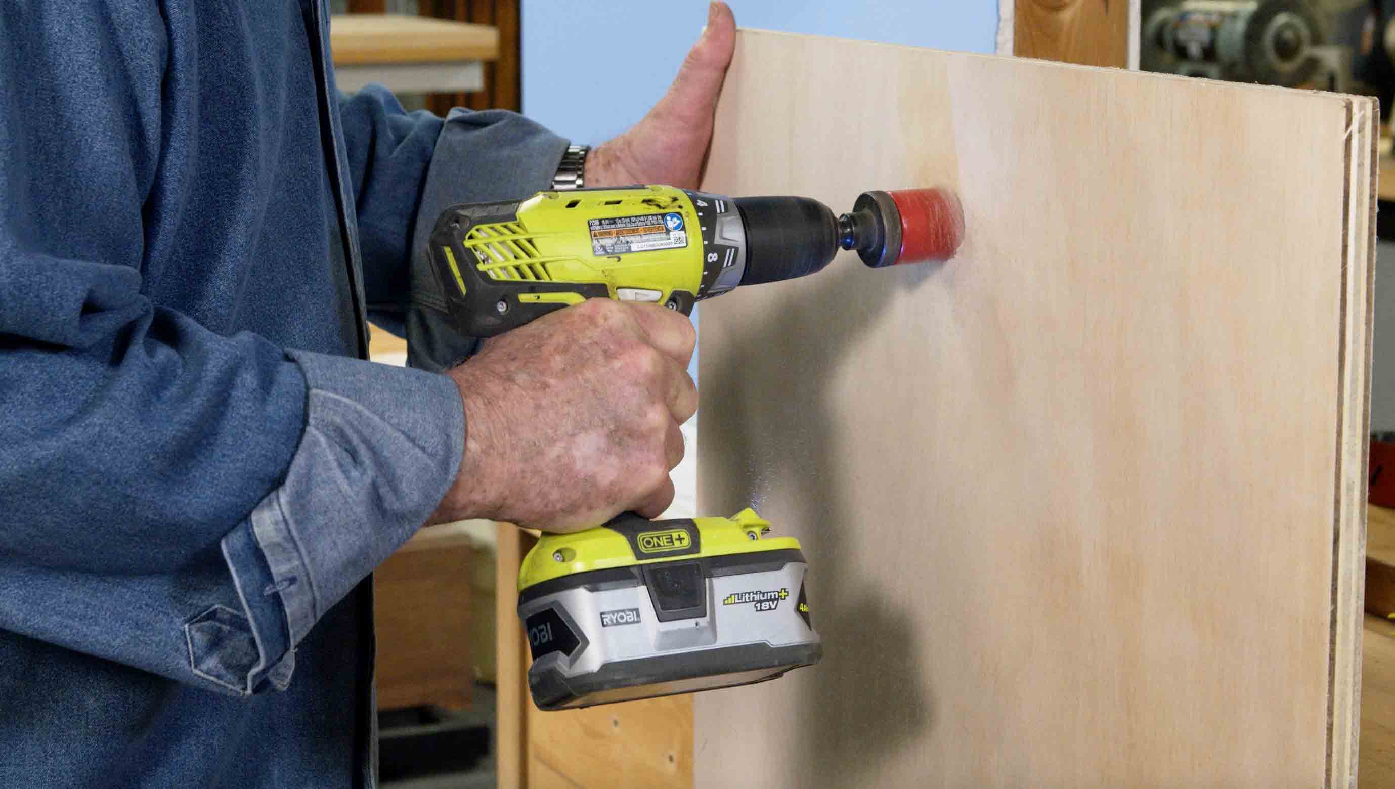 Man uses a hole saw to cut a hole in wood 