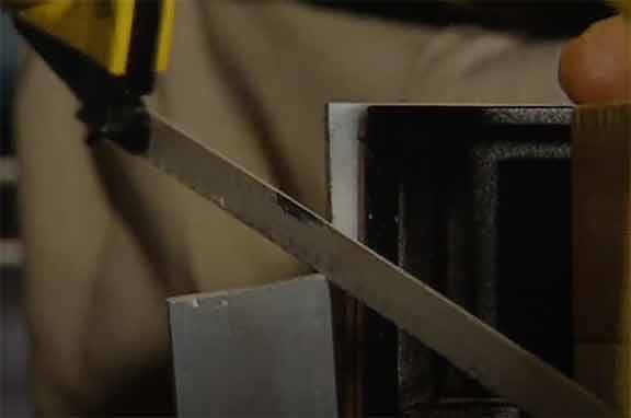 Man uses a hacksaw with a light duty blade to cut through aluminum metal sheet