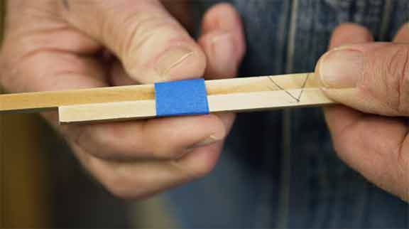 Man holds 2 pieces of wood together with masking tape