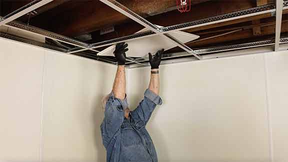 Man installs ceiling tiles into metal framework