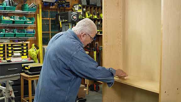 Man using piece of wood to measure inside of cabinet