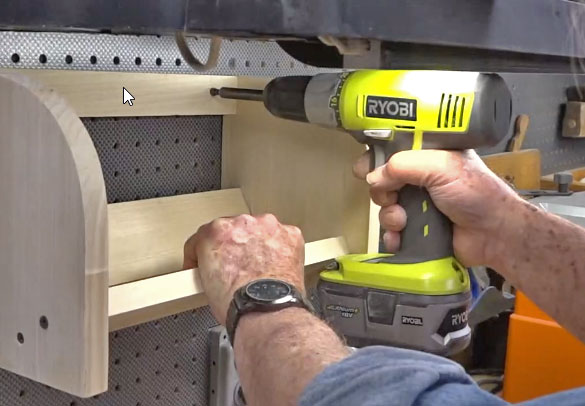 Man using a Ryobi drill to fasten a wooden tape caddy to workshop bench 