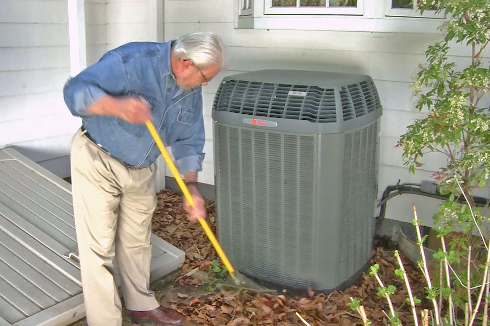 Man raking leaves away from air conditioner condenser