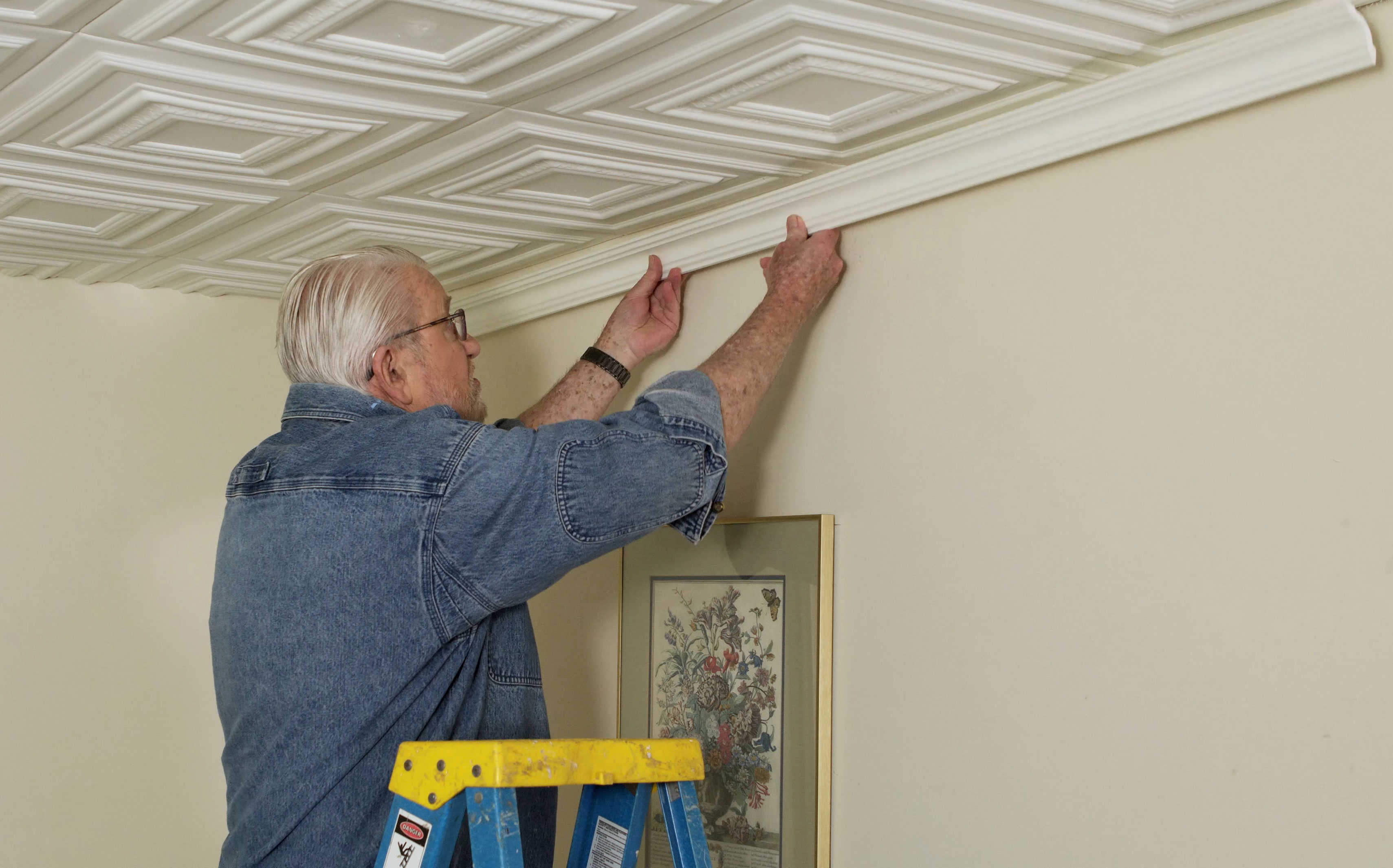 Man installing crown molding on foam tile ceiling 